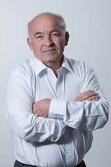 Image showing Confident senior man in white shirt crossing hands on chest and looking at camera while standing against gray background. Self confident senior isolated white studio shoot.