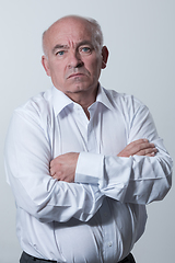 Image showing Confident senior man in white shirt crossing hands on chest and looking at camera while standing against gray background. Self confident senior isolated white studio shoot.