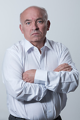 Image showing Confident senior man in white shirt crossing hands on chest and looking at camera while standing against gray background. Self confident senior isolated white studio shoot.