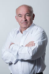 Image showing Confident senior man in white shirt crossing hands on chest and looking at camera while standing against gray background. Self confident senior isolated white studio shoot.