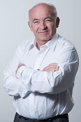 Image showing Confident senior man in white shirt crossing hands on chest and looking at camera while standing against gray background. Self confident senior isolated white studio shoot.