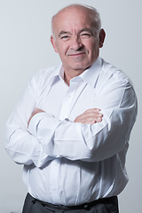 Image showing Confident senior man in white shirt crossing hands on chest and looking at camera while standing against gray background. Self confident senior isolated white studio shoot.