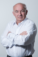 Image showing Confident senior man in white shirt crossing hands on chest and looking at camera while standing against gray background. Self confident senior isolated white studio shoot.