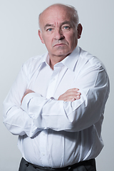 Image showing Confident senior man in white shirt crossing hands on chest and looking at camera while standing against gray background. Self confident senior isolated white studio shoot.