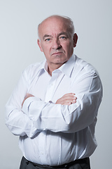 Image showing Confident senior man in white shirt crossing hands on chest and looking at camera while standing against gray background. Self confident senior isolated white studio shoot.