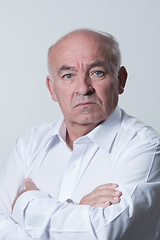 Image showing Confident senior man in white shirt crossing hands on chest and looking at camera while standing against gray background. Self confident senior isolated white studio shoot.