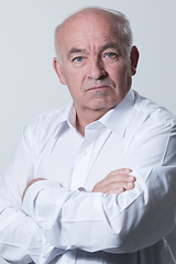 Image showing Confident senior man in white shirt crossing hands on chest and looking at camera while standing against gray background. Self confident senior isolated white studio shoot.