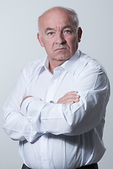 Image showing Confident senior man in white shirt crossing hands on chest and looking at camera while standing against gray background. Self confident senior isolated white studio shoot.