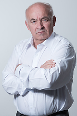 Image showing Confident senior man in white shirt crossing hands on chest and looking at camera while standing against gray background. Self confident senior isolated white studio shoot.