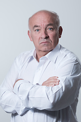 Image showing Confident senior man in white shirt crossing hands on chest and looking at camera while standing against gray background. Self confident senior isolated white studio shoot.