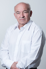 Image showing Portrait of an older man wearing a white shirt on a gray background. A healthy old man looks at a camera isolated over a gray wall. An older man smiles at the camera, a happy old man.