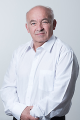 Image showing Portrait of an older man wearing a white shirt on a gray background. A healthy old man looks at a camera isolated over a gray wall. An older man smiles at the camera, a happy old man.