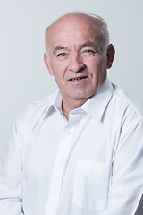 Image showing Portrait of an older man wearing a white shirt on a gray background. A healthy old man looks at a camera isolated over a gray wall. An older man smiles at the camera, a happy old man.