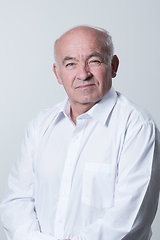 Image showing Portrait of an older man wearing a white shirt on a gray background. A healthy old man looks at a camera isolated over a gray wall. An older man smiles at the camera, a happy old man.