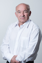 Image showing Portrait of an older man wearing a white shirt on a gray background. A healthy old man looks at a camera isolated over a gray wall. An older man smiles at the camera, a happy old man.