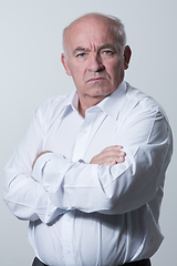 Image showing Confident senior man in white shirt crossing hands on chest and looking at camera while standing against gray background. Self confident senior isolated white studio shoot.