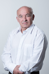 Image showing Portrait of an older man wearing a white shirt on a gray background. A healthy old man looks at a camera isolated over a gray wall. An older man smiles at the camera, a happy old man.