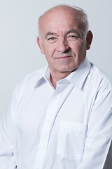 Image showing Portrait of an older man wearing a white shirt on a gray background. A healthy old man looks at a camera isolated over a gray wall. An older man smiles at the camera, a happy old man.