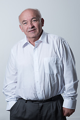 Image showing Portrait of an older man wearing a white shirt on a gray background. A healthy old man looks at a camera isolated over a gray wall. An older man smiles at the camera, a happy old man.