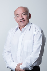 Image showing Portrait of an older man wearing a white shirt on a gray background. A healthy old man looks at a camera isolated over a gray wall. An older man smiles at the camera, a happy old man.