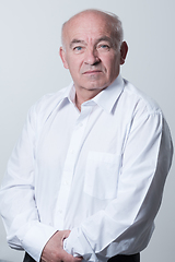 Image showing Portrait of an older man wearing a white shirt on a gray background. A healthy old man looks at a camera isolated over a gray wall. An older man smiles at the camera, a happy old man.