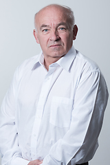 Image showing Portrait of an older man wearing a white shirt on a gray background. A healthy old man looks at a camera isolated over a gray wall. An older man smiles at the camera, a happy old man.