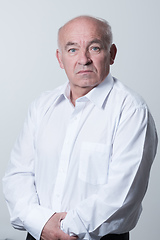 Image showing Portrait of an older man wearing a white shirt on a gray background. A healthy old man looks at a camera isolated over a gray wall. An older man smiles at the camera, a happy old man.