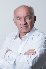 Image showing Confident senior man in white shirt crossing hands on chest and looking at camera while standing against gray background. Self confident senior isolated white studio shoot.