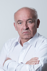 Image showing Confident senior man in white shirt crossing hands on chest and looking at camera while standing against gray background. Self confident senior isolated white studio shoot.