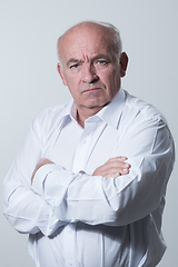 Image showing Confident senior man in white shirt crossing hands on chest and looking at camera while standing against gray background. Self confident senior isolated white studio shoot.