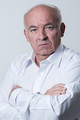 Image showing Confident senior man in white shirt crossing hands on chest and looking at camera while standing against gray background. Self confident senior isolated white studio shoot.