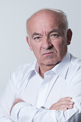 Image showing Confident senior man in white shirt crossing hands on chest and looking at camera while standing against gray background. Self confident senior isolated white studio shoot.