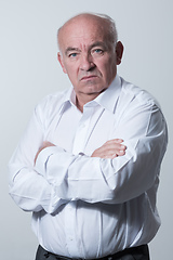 Image showing Confident senior man in white shirt crossing hands on chest and looking at camera while standing against gray background. Self confident senior isolated white studio shoot.