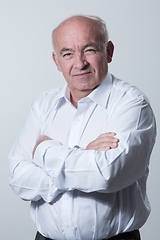 Image showing Confident senior man in white shirt crossing hands on chest and looking at camera while standing against gray background. Self confident senior isolated white studio shoot.