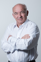 Image showing Confident senior man in white shirt crossing hands on chest and looking at camera while standing against gray background. Self confident senior isolated white studio shoot.