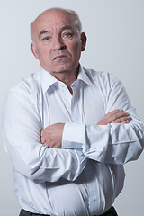 Image showing Confident senior man in white shirt crossing hands on chest and looking at camera while standing against gray background. Self confident senior isolated white studio shoot.