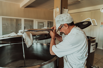 Image showing Man mixing milk in the stainless tank during the fermentation process at the cheese manufacturing