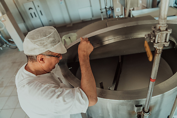 Image showing Man mixing milk in the stainless tank during the fermentation process at the cheese manufacturing