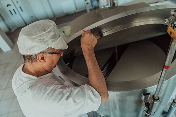 Image showing Man mixing milk in the stainless tank during the fermentation process at the cheese manufacturing