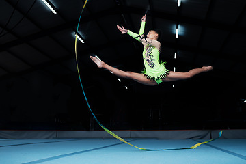 Image showing Jump, rhythmic gymnastics and woman in gym with ribbon, creative sport or action, performance or fitness. Competition, athlete and female gymnast, dance and art with body, routine and energy at arena