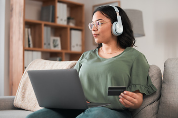Image showing Woman, laptop and credit card with headphones and online shopping on sofa, music subscription payment and fintech. Female customer at home, thinking of finance with e commerce and podcast membership