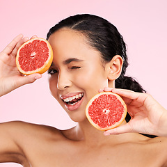 Image showing Face, beauty and woman wink with grapefruit in studio isolated on a pink background. Portrait, natural cosmetic and model with fruit, food or nutrition for skincare, healthy vegan diet or vitamin c