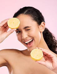 Image showing Woman, beauty and lemon for wink in studio portrait, smile and natural skin glow by pink background. Latino girl, model and fruit for cosmetics, eye emoji and detox for wellness, nutrition and shine