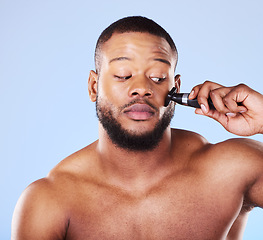 Image showing Man, shave and worry with face razor for hair removal, aesthetic skincare and facial cleaning in studio. Scared black male model shaving beard with blade, trimmer or cosmetic tool on blue background