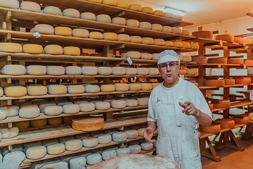 Image showing A worker at a cheese factory sorting freshly processed cheese on drying shelves