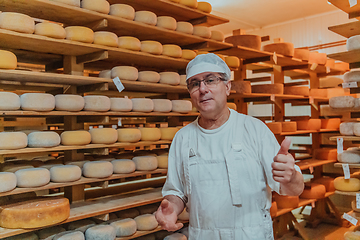 Image showing A worker at a cheese factory sorting freshly processed cheese on drying shelves