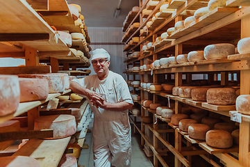 Image showing A worker at a cheese factory sorting freshly processed cheese on drying shelves