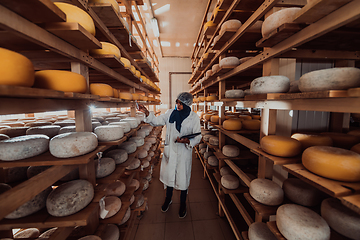 Image showing African American Muslim businesswoman checking product quality and entering data into a laptop at a local cheese manufacturing company