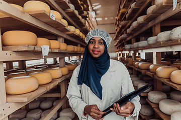 Image showing African American Muslim businesswoman checking product quality and entering data into a laptop at a local cheese manufacturing company