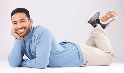 Image showing Portrait, happy or Asian man lying on floor isolated on a white background in studio to relax. Friendly smile, calm person or proud male model resting with confidence, fashion or style on the ground